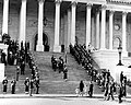 Body bearers carrying the casket of President Kennedy up the center steps of the United States Capitol Building, followed by a color guard holding the flag of the President of the United States, and the late President's widow, Jacqueline Kennedy and her children, Caroline Kennedy and John F. Kennedy, Jr., on November 24, 1963.